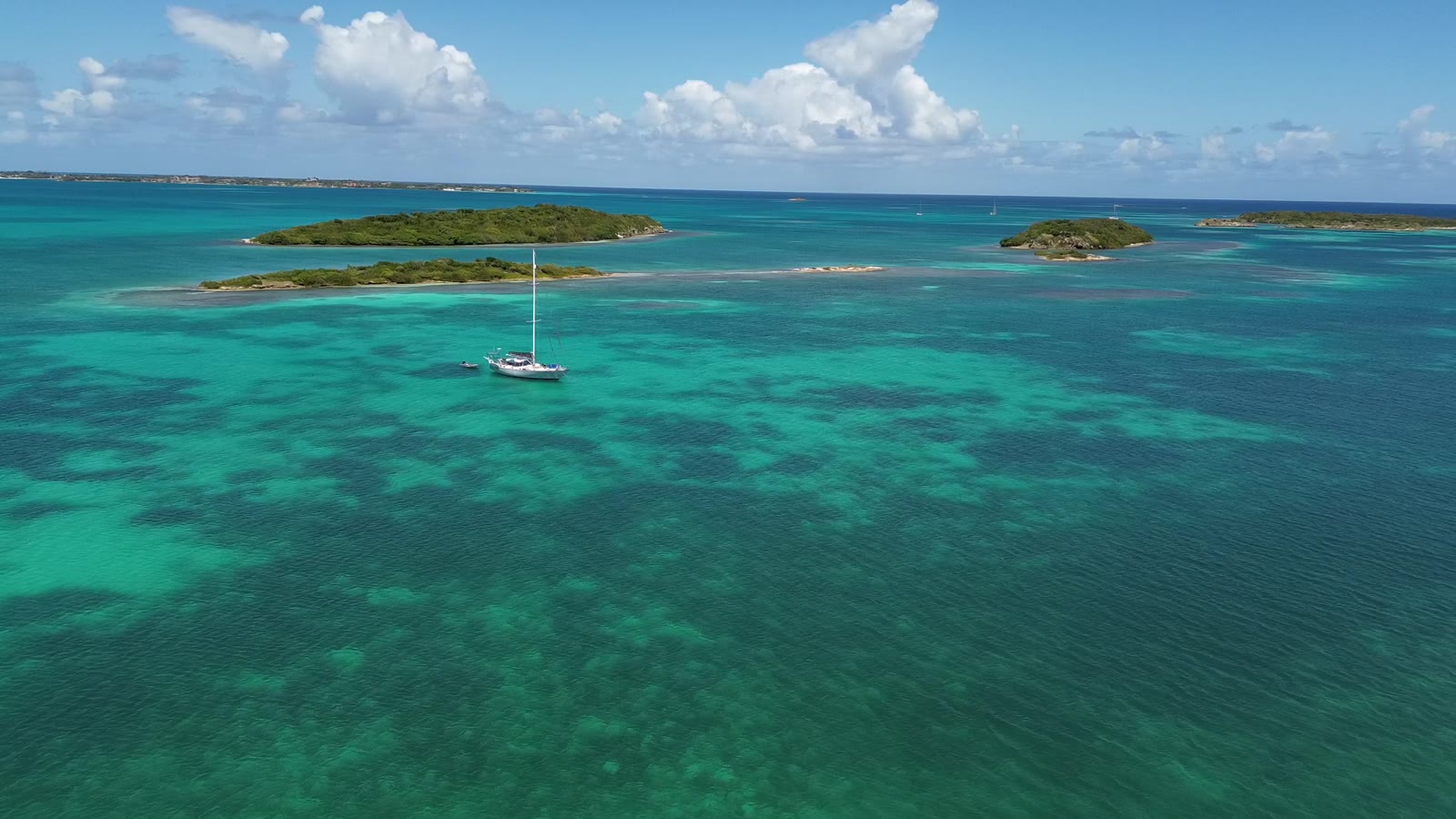 Aerial view of a sailing yacht anchored alone in turquoise water among reefs and low islands in Antigua