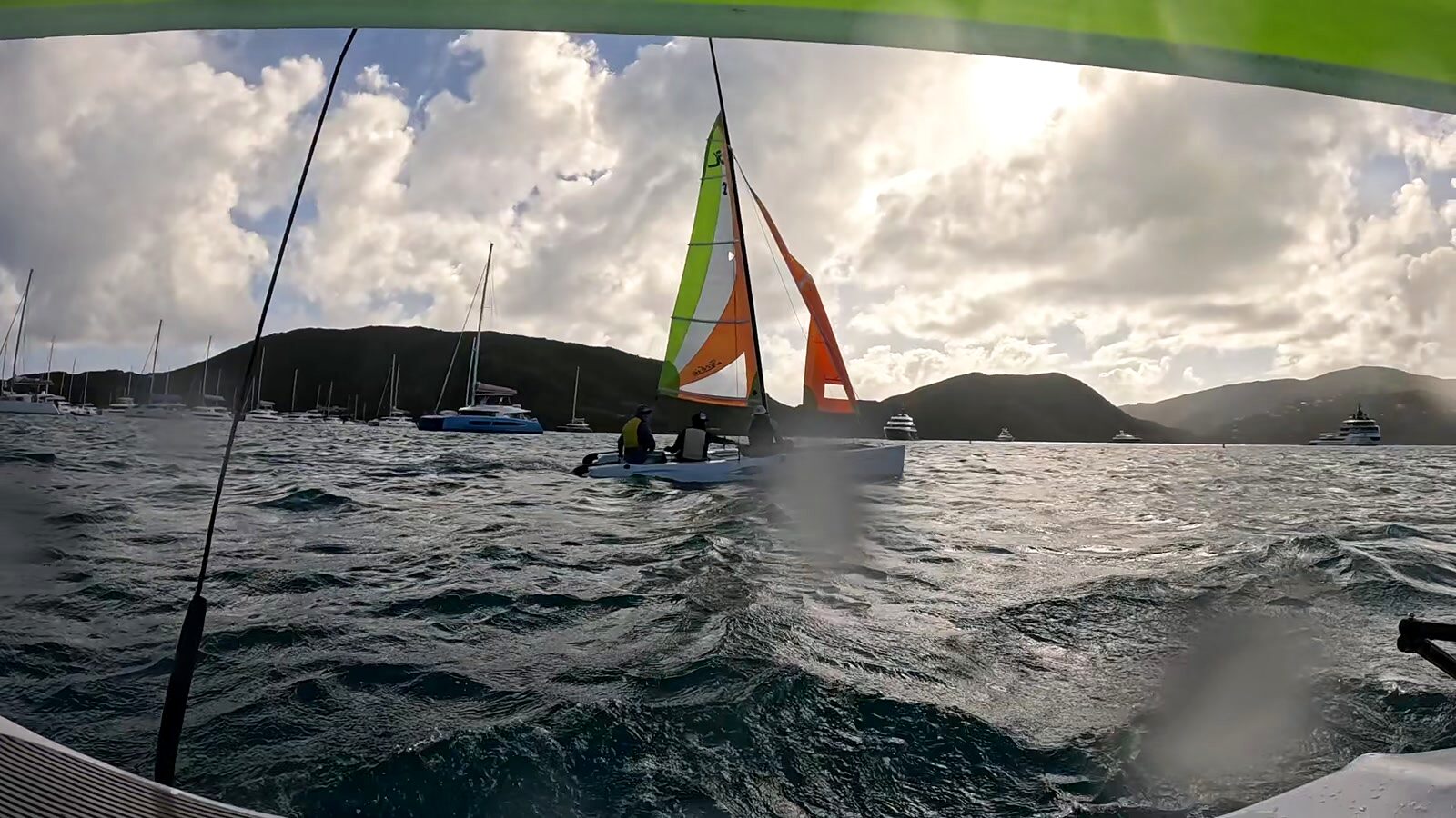 A small sailing dinghy crossing North Sound past moored catamarans near Bitter End