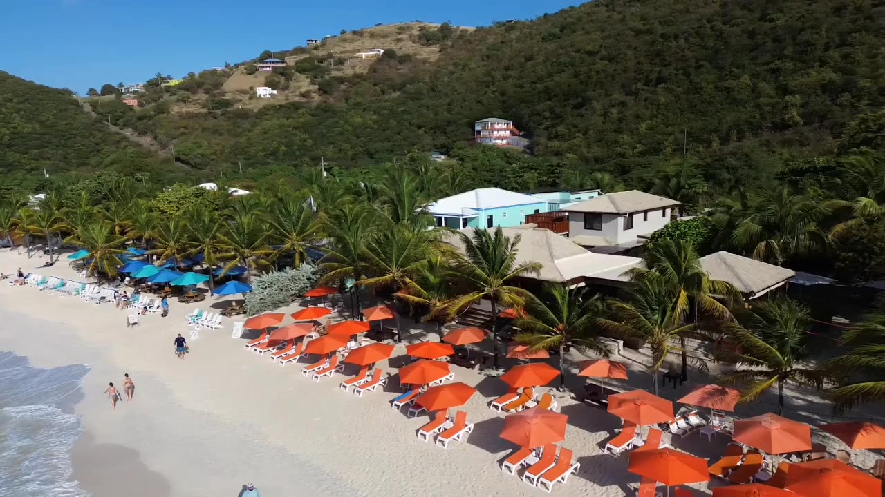 Orange umbrellas and sun loungers on the sand in front of Gertrude's Beach Bar at White Bay, Jost Van Dyke, seen from a drone