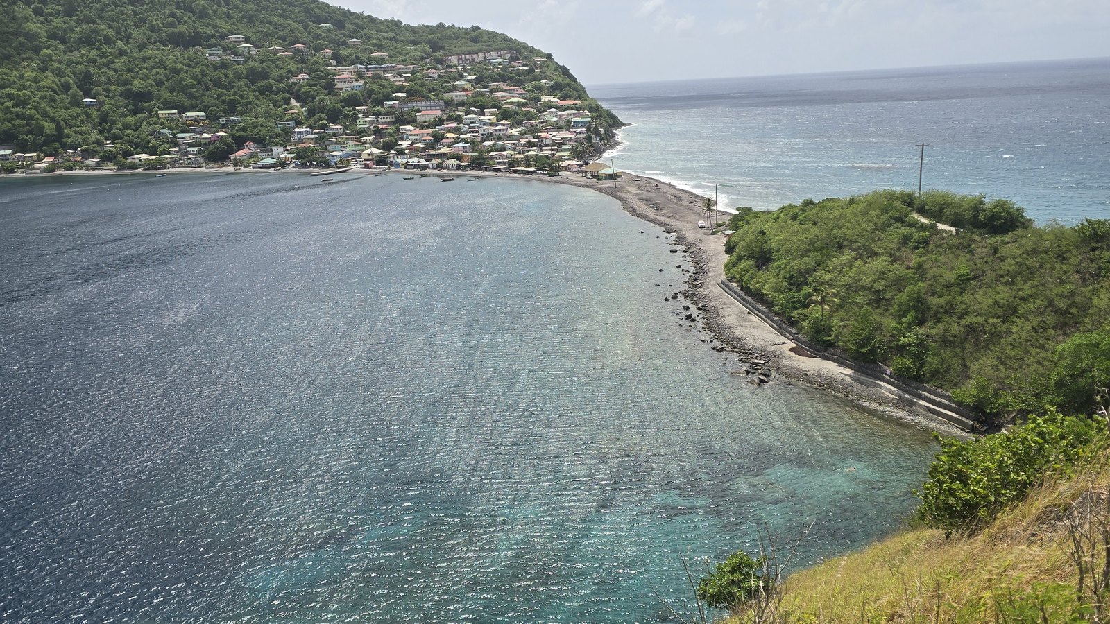 The narrow isthmus at Scotts Head with clear turquoise water of Soufriere Bay on one side and the village climbing the green hillside behind, at the south tip of Dominica