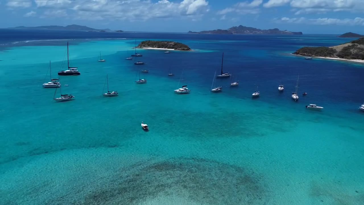 Yachts at anchor in turquoise water between the small islands of the Tobago Cays in the Grenadines, seen from a drone
